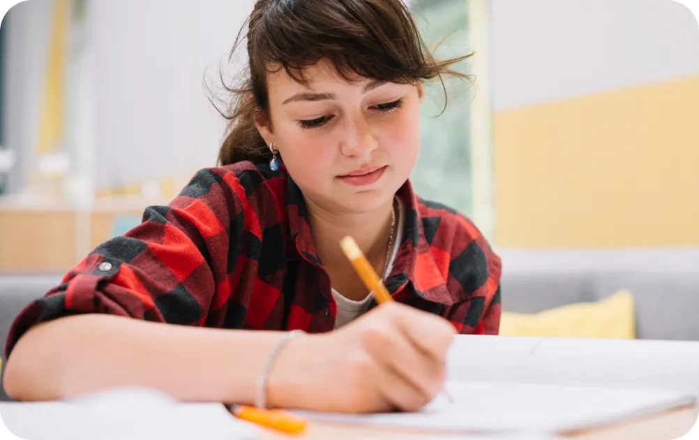 Teen girl writing in a notebook with a pencil, focused on studies